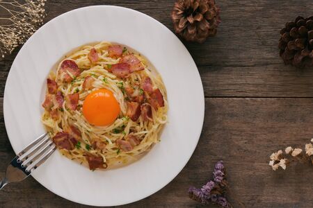 Spaghetti carbonara with bacon, cheese, yolk and chopped parsley on wood table in top view flat lay with copy space. Italian traditional homemade food for lunch or dinner so creamy and delicious.の写真素材