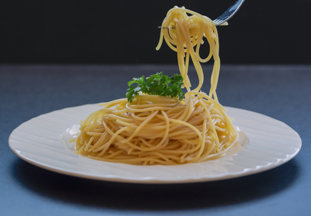 Boiled spaghetti with al dente level. Cooked pasta prepared for cooking on white plate decorated with parsley in close up view with copy space on wood table. Homemade Italian traditional food concept.の写真素材