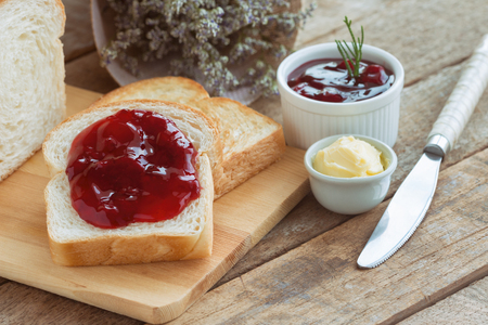 Delicious toast bread served with butter and spread with strawberry jam on wood cutting board put on rustic wooden table with copy space. Homemade bakery concept. American breakfast style.の写真素材