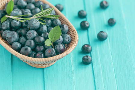 Fresh ripe wild blueberries in wooden basket on blue wood table in top view with copy space for background. Blueberry is antioxidant food and vitamin C. Healthy and delicious fruits concept.の写真素材
