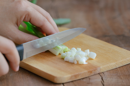 Woman use knife kitchen and wood cutting board to chopped or cut and sliced fresh scallions or spring onion to shredded prepare for soup cooking in the morning. Homemade cooking concept.の写真素材
