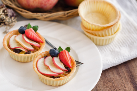 Homemade bakery apple caramel tart decorated with sliced apple strawberry and blueberry on white plate put on wood table. Delicious and sweet pastry ready to served for coffee break or afternoon tea.の写真素材
