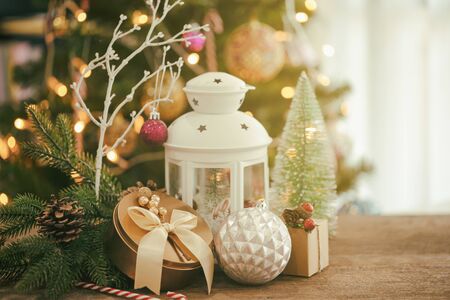 Christmas decoration with white lantern, luxury golden gift box, candy cane, cute ball, pine leaves and cones on wood table with copy space. Bokeh Christmas tree wallpaper for xmas celebration.の写真素材