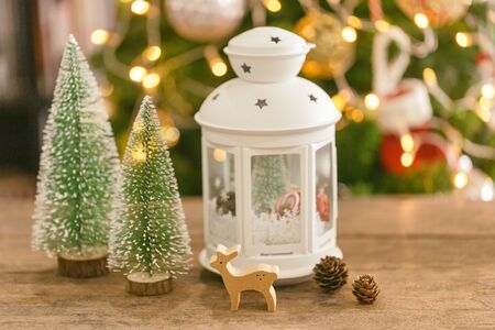 Christmas background decoration with sweet white lantern, pine leaves, pine cones and bauble wooden reindeer on wood table with copy space. Bokeh Christmas tree wallpaper for xmas celebration.の写真素材