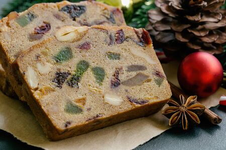 Sweet fruit cake slices on brown paper put on black granite table in close up view with Christmas decoration. Traditional rum fruit cake for Christmas celebrate festival. Homemade bakery concept.の写真素材