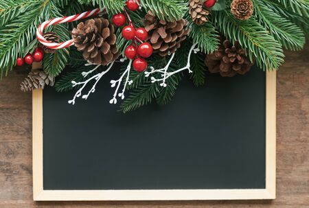 Christmas decoration background with blackboard or chalkboard, pine leaves and cones and holly balls on wood table with copy space in top view flat lay.Vintage Christmas wallpaper for xmas celebrationの写真素材