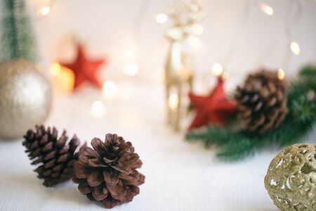 Pine cone or conifer cones near red star shape and golden bubble ball on white wood plank with golden light bokeh backdrop. Sweet background for Christmas and winter season wallpaper with copy space.の写真素材