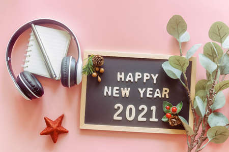Wooden alphabet on wood letter board in words Happy New Year 2021 on pastel pink background with stationery, leaf, red star and headphone in top view flat lay. New year season greetings concept.の写真素材