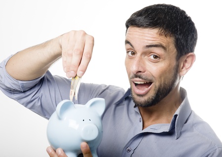 Handsome Young Man with Beard putting Money in Blue Piggy bank Isolated on White Backgroundの写真素材