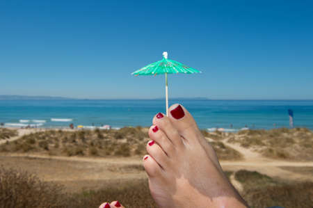 feet relaxing at the beach taking shade from a cocktail umbrella. の写真素材