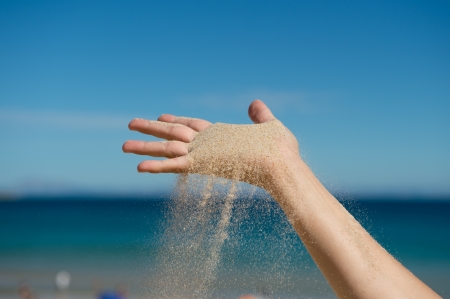 Sand grains falling for a caucasian hand at the beach blue backgroundの写真素材
