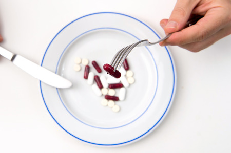 Medical Meal, Man hands with fork and Knife eating Tablets and Pills on a plateの写真素材