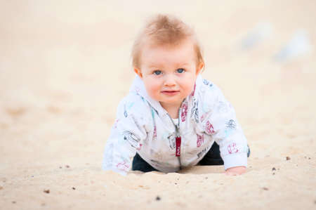 Little blonde kid playing on Beach lying on Sand and Seagullsの写真素材