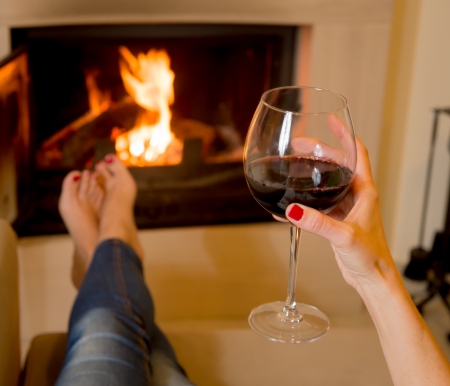 Woman holding a glass of red wine sitting in front of an open fireの写真素材