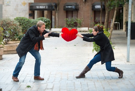 young attractive couple fighting over a love hearted shaped pillow の写真素材