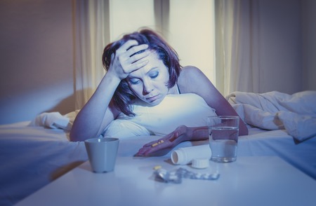 red haired woman sick with flu or cold in bed with water and medicine in the foreground の写真素材