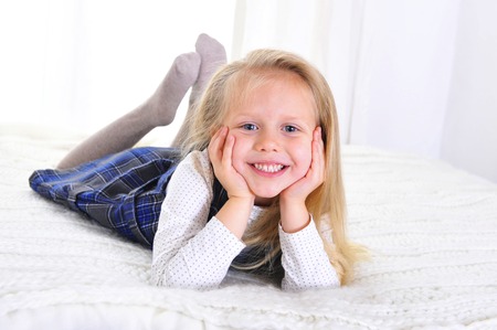 Adorable blonde blue eyed little girl lying happy on bed isolated on white background