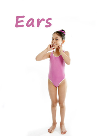 full length of girl wearing a pink swimsuit pointing at her ears on a white background for a school anatomy or body part chartの写真素材