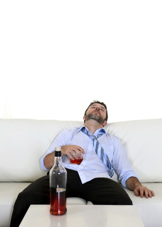 Attractive drunk business man lying asleep on couch at living room sleeping wasted holding whiskey glass in alcoholism problem , alcohol abuse and addiction concept looking messy and sickの写真素材