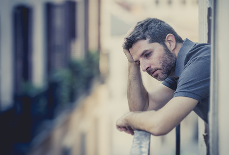 young man alone outside at house balcony terrace looking depressed, destroyed, wasted and sad suffering emotional crisis and depression on urban background の写真素材