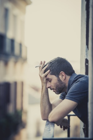 young man alone outside at house balcony terrace smoking depressed, destroyed, wasted and sad suffering emotional crisis and depression on urban の写真素材