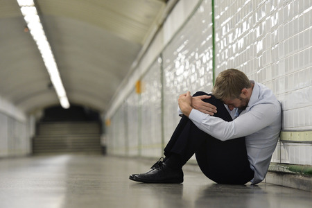 Young business man who lost job abandoned lost in depression sitting on ground street subway suffering emotional pain, thinking and leaning on wall aloneの写真素材