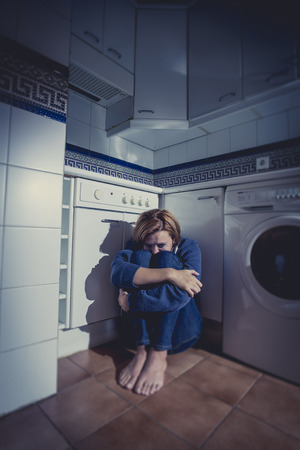 lonely depressed and sick woman sitting alone on kitchen floor in stress , depression and sadness feeling miserable in barefoot looking desperate hugging or holding her kneesの写真素材