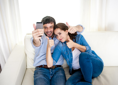 nice attractive young couple sitting together in sofa couch taking selfie photo with mobile phone...