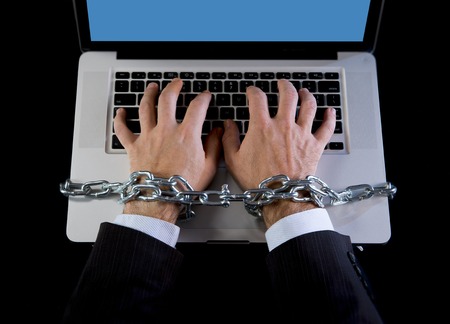 Hands of caucasian businessman addicted to work tied and bond with iron chain handcuffed to computer laptop in workaholic, internet slave and addict conceptの写真素材