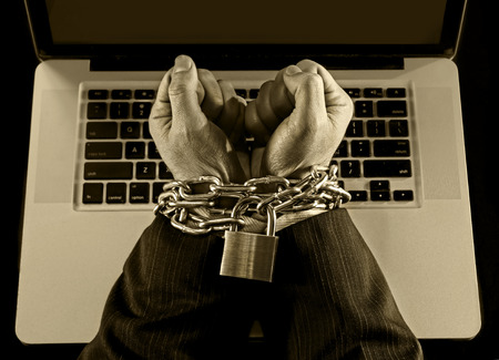 Hands of caucasian businessman addicted to work tied and bond with iron chain handcuffed to computer laptop in workaholic, internet slave and addict concept in black and whiteの写真素材