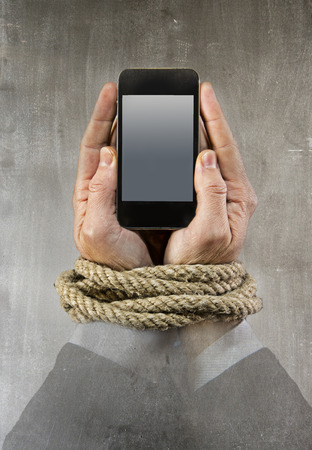 Hands of businessman addicted to mobile phone rope bond wrists in smartphone internet addiction and slave to online network addict concept isolated black backgroundの写真素材