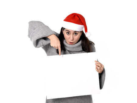 young attractive Hispanic woman wearing Santa Claus Christmas hat and winter jumper holding and pointing blank billboard or placard sign as copy space adding corporate marketing isolated on white backgroundの写真素材