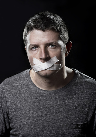 attractive young man with mouth sealed on duct tape to prevent him from speaking keeping him mute and censored in freedom of speech and expression conceptの写真素材