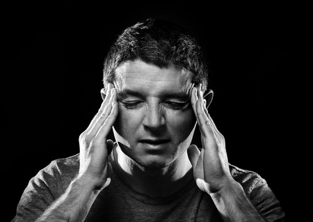 young man suffering migraine and headache in intense pain feeling desperate and sick with hands on tempo isolated on studio background black and whiteの写真素材