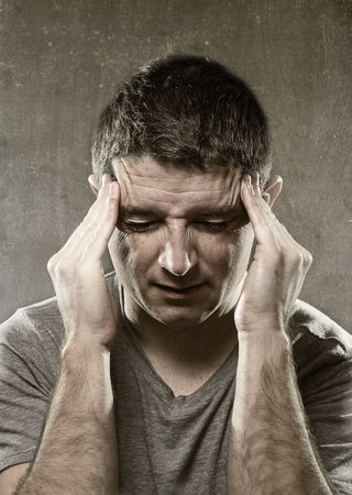 young man suffering migraine and headache in intense pain feeling desperate and sick with hands on tempo isolated on grunge studio backgroundの写真素材