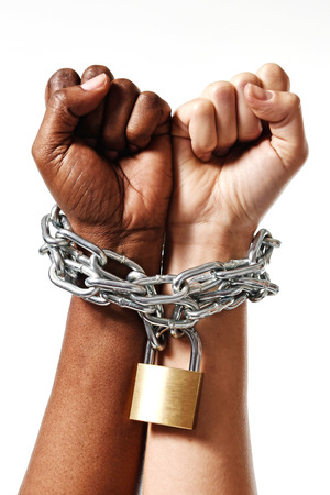 white Caucasian hand chained with iron chain and locked together with black ethnicity female around wrists in togetherness, multiracial respect and understanding conceptの写真素材
