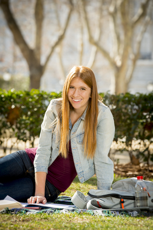 young beautiful student girl lying on campus park grass with books on rug studying happy preparing exam in university and college education conceptの写真素材