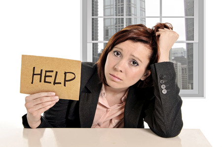 sad businesswoman in stress at office work asking for help sitting frustrated and depressed in front of business district window view pulling her red hairの写真素材
