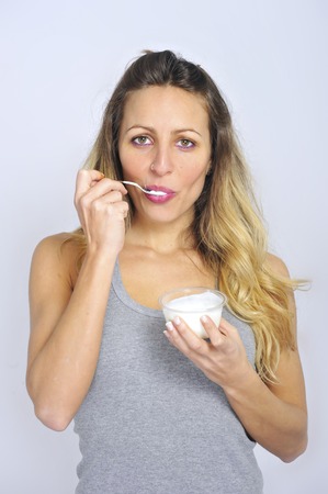 young sexy and attractive blond hair girl with spoon happy and fit eating natural cream yogurt in...