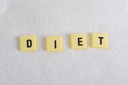 diet block letters in crossword over sugar pile isolated on sweet grainy white sugar texture in sugar excess, dieting and healthy nutrition conceptの写真素材