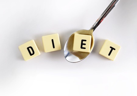 diet block word in crossword over sugar pile with spoon taking one letter  isolated on sweet grainy white sugar texture in sugar excess, dieting and healthy nutrition conceptの写真素材