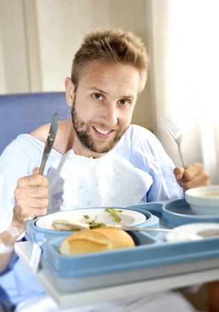 young patient man in hospital room after suffering accident eating the healthy diet clinic food in happy and satisfied face expression enjoying the medical center mealの写真素材