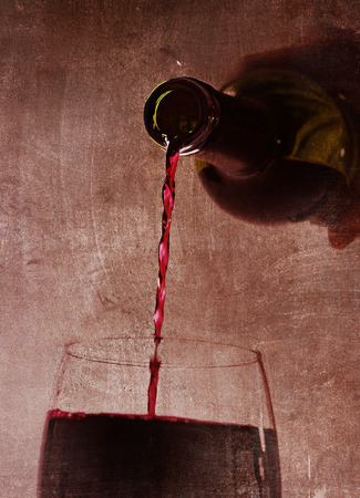 Close up view of Man hand holding Bottle pouring Spanish red wine filling Glass on a dark grunge arty background in luxury gourmet and expensive winery conceptの写真素材