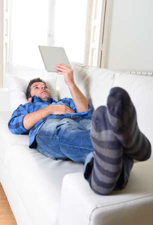 young attractive 30s man using digital tablet pad lying on couch at home living room networking looking relaxed and happy in portable technology and internet conceptの写真素材