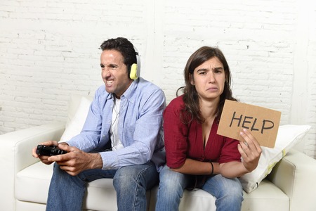 young attractive woman asking for help angry and upset while husband or boyfriend plays videogames ignoring her in technology and gaming addiction conceptの写真素材