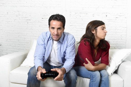 young attractive woman bored angry frustrated and upset while husband or boyfriend plays videogames ignoring her in technology and gaming addiction conceptの写真素材