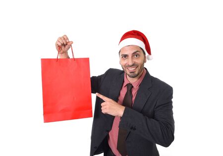 young attractive businessman in Christmas Santa hat holding and pointing red shopping bag in December and New year sale and market opportunity concept performing as salesman or customer isolated on white backgroundの写真素材