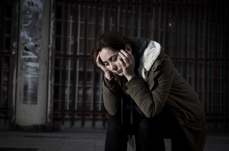 young woman alone on street suffering depression looking sad desperate and helpless sitting lonely in dirty dark urban night background in female victim of abuse conceptの写真素材