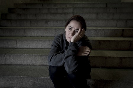 sad woman alone on street subway staircase suffering depression looking sick and helpless sitting lonely as female victim of abuse concept  in  dark urban night grunge backgroundの写真素材