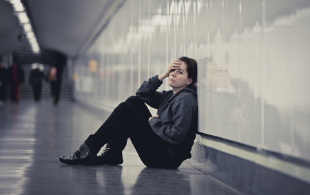 young sad woman in pain sitting alone and depressed at urban subway tunnel ground looking worried and frustrated covering her face suffering depression in female loneliness conceptの写真素材